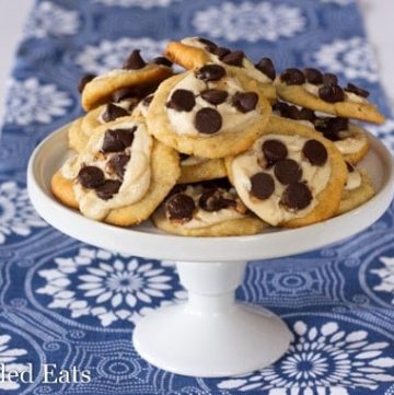 pile of two bite chocolate chip cheese danishes on a white cake plate set on a decorative blue table cloth