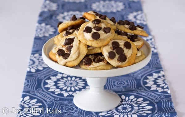 pile of two bite chocolate chip cheese danishes on a white cake plate set on a decorative blue table cloth