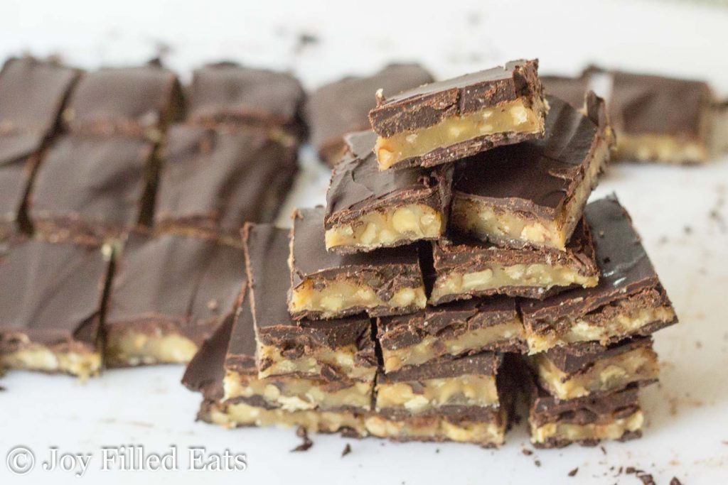 A stack of Buttery Walnut Homemade Toffee Candy cut into squares on a white cutting board