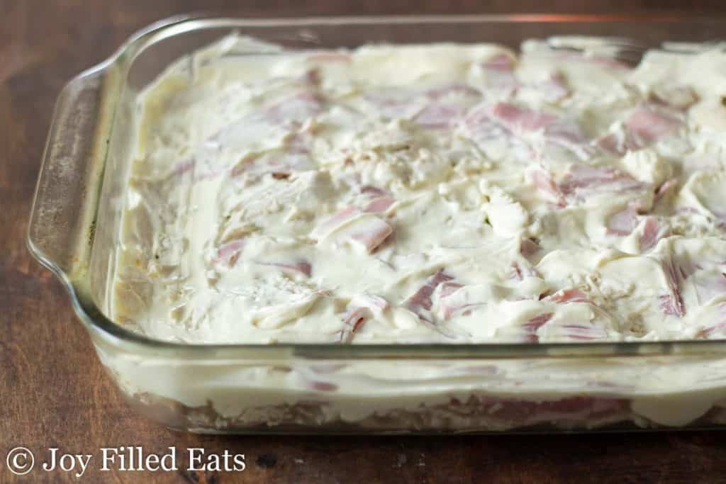 creamy cheese sauce layered onto chicken and ham pieces on casserole dish