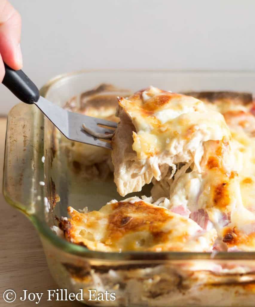 hand holding a serving spatula lifting a portion of chicken cordon bleu casserole from dish