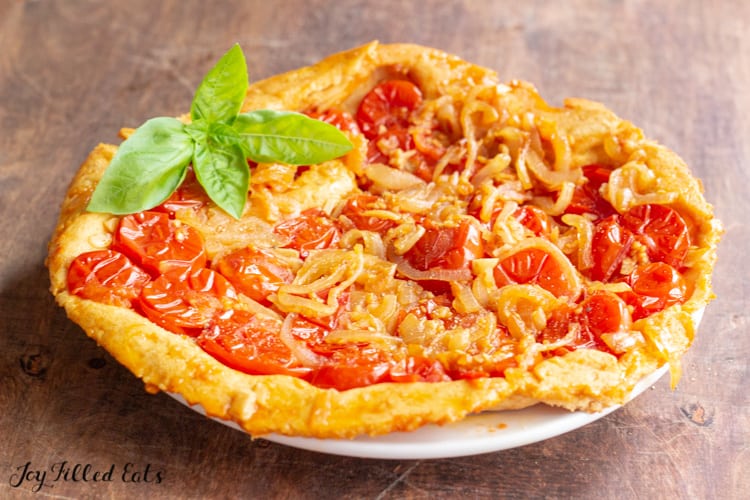 tomato tart garnished with basil on a white plate