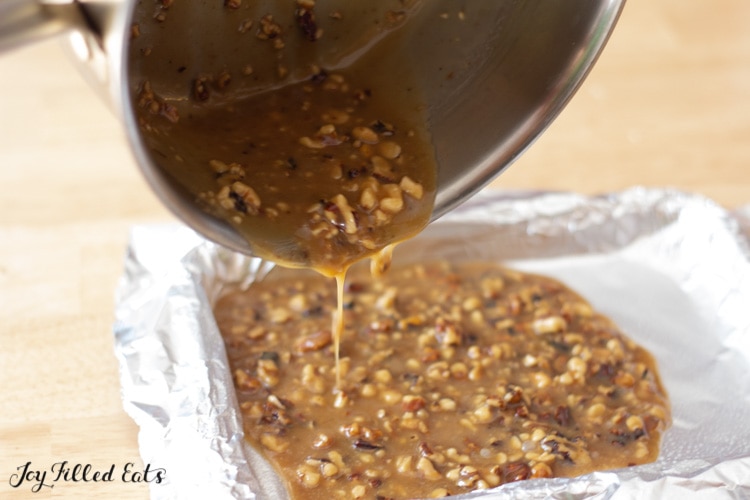 saucepan pouring walnut toffee mixture into a aluminum lined sheet pan