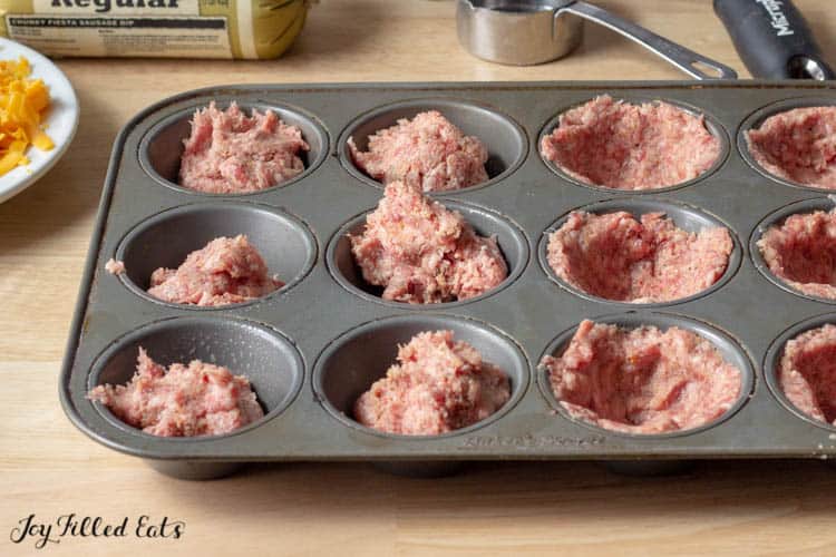 Muffin Tin with sausage meat in mold. Half shaped into sausage cup, half balls of sausage meat