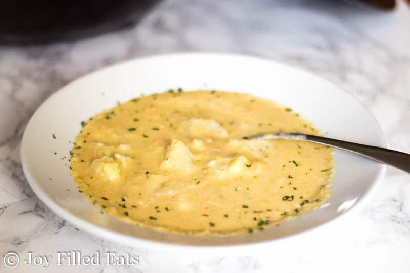 shallow bowl full of creamy cauliflower soup with a spoon