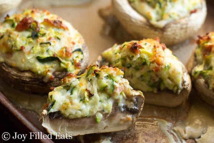 two halves of a stuffed mushroom with bacon and cheese on a sheet pan surrounded by other stuffed mushrooms