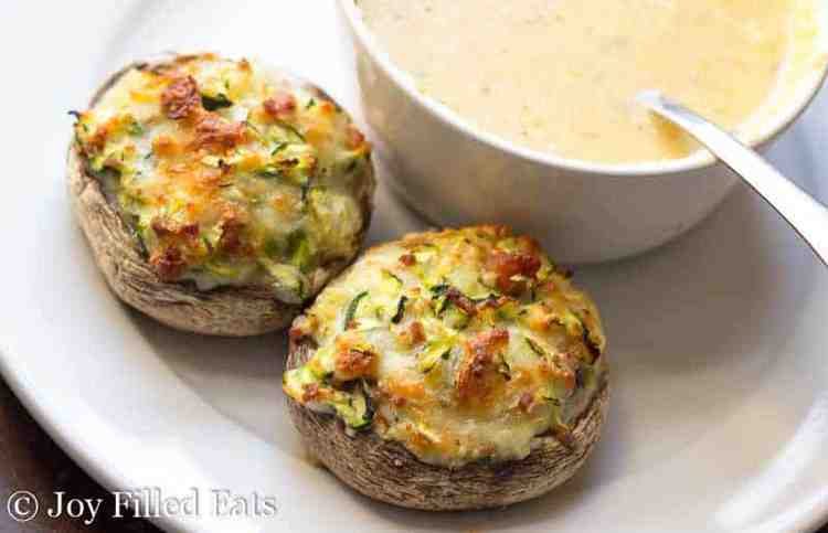 two cheese stuffed mushrooms with bacon on a white plate next to a bowl full of soup