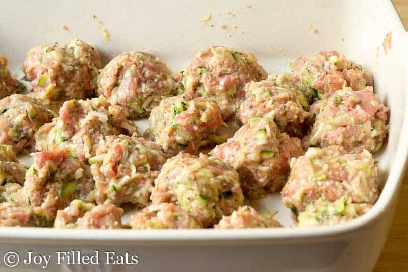 raw meatballs lined on a the bottom of a white casserole dish close up
