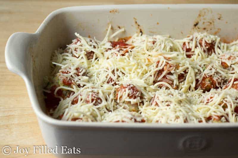 shredded cheese covering meatballs and sauce layered in a white casserole dish