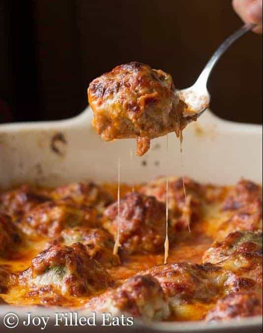 hand holding spoon lifting a single meatball from the casserole dish of easy meatball Parmesan casserole