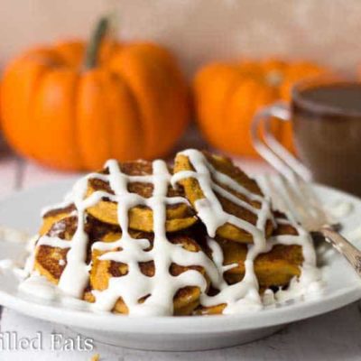 pile of pumpkin roll pancakes drizzled in a cream cheese icing on a white plate with fork