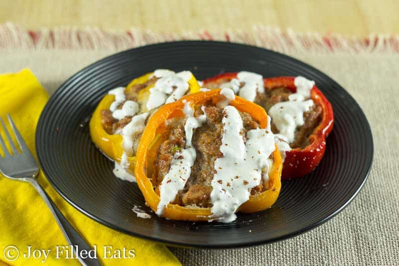 taco stuffed pepper rings drizzled with sour cream on a black plate next to a yellow napkin and fork