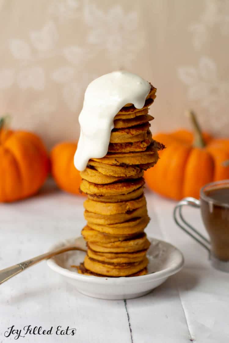 large stack of keto pumpkin pancakes topped with a cream cheese icing dripping down the side of the stack
