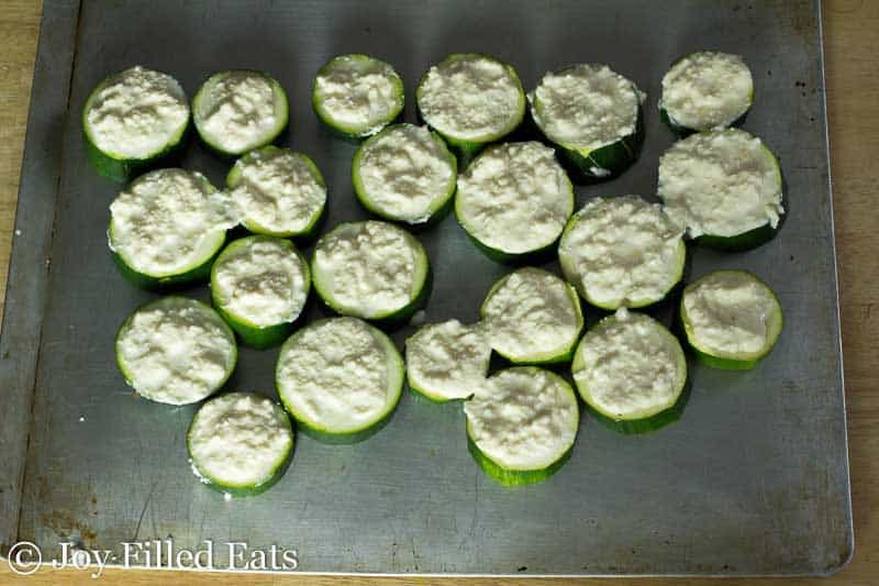 overhead view of zucchini rounds topped with a Parmesan cheese spread arranged on a cookie sheet