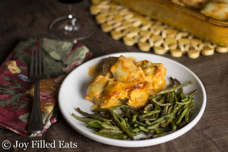 green beans and a portion of creamy tomato chicken and spaghetti squash casserole on a white plate set on a table setting with decorative napkin and fork