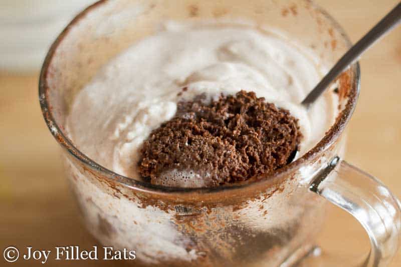 close up on glass mug filled with chocolate chocolate chip cannoli mug cake with spoon lifting bite of cake from mug