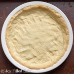 overhead view of low carb pie crust pressed into a white pie plate and punctured with fork holes