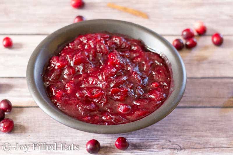 small jar of sugar free cranberry sauce surrounded by scattered cranberries on the table