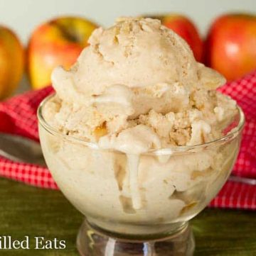 scoop of apple pie ice cream in a glass bowl set in front of a row of apples