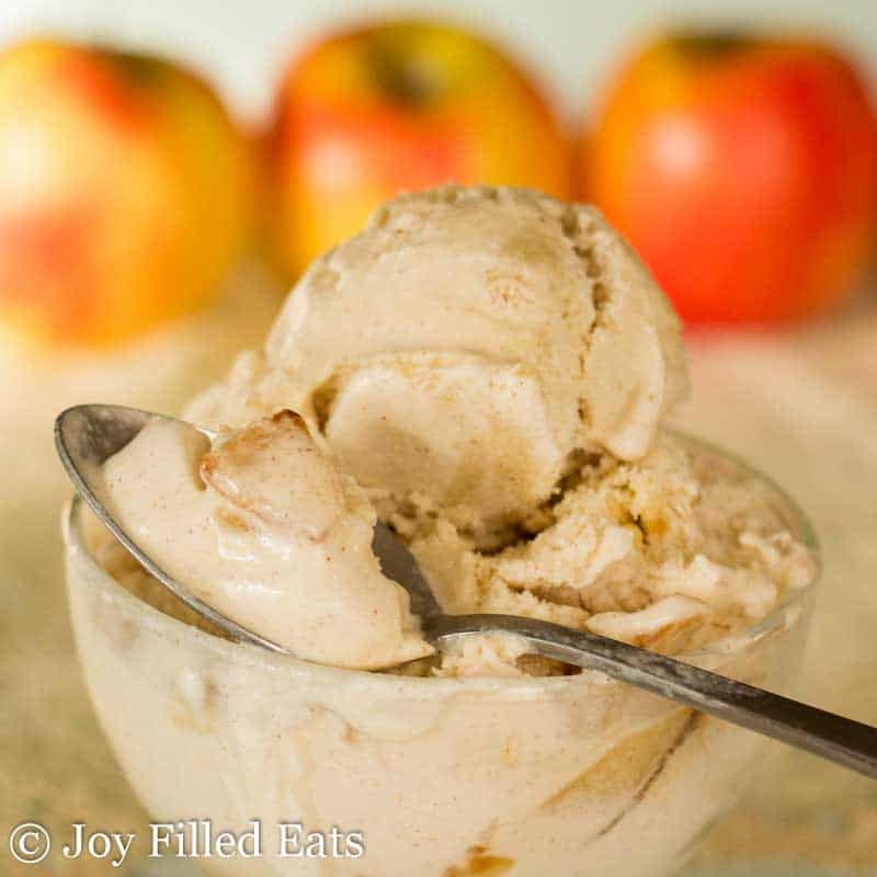 scoop of apple pie ice cream on a spoon resting on the rim of a glass bowl with a large scoop of ice cream in the bowl