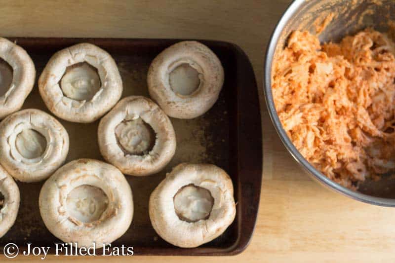 pizza chicken filling in a large mixing bowl set next to a sheet pan lined with mushrooms caps