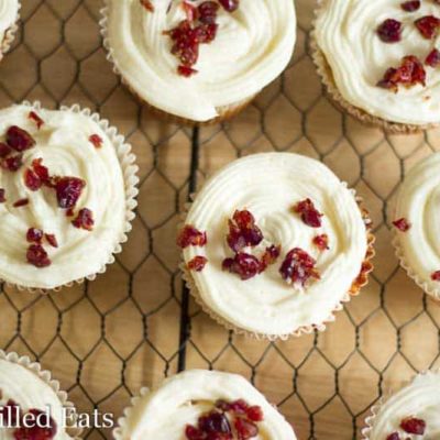 overhead view of cranberry cupcakes with cream cheese icing topped with dried cranberries set on a cooling rack