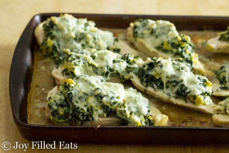 baking pan lined with cooked chicken pieces and topped with spinach, artichoke and melted cheese topping