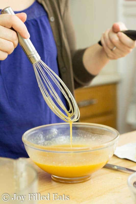 hand holding a whisk and mixing eggs in a glass bowl
