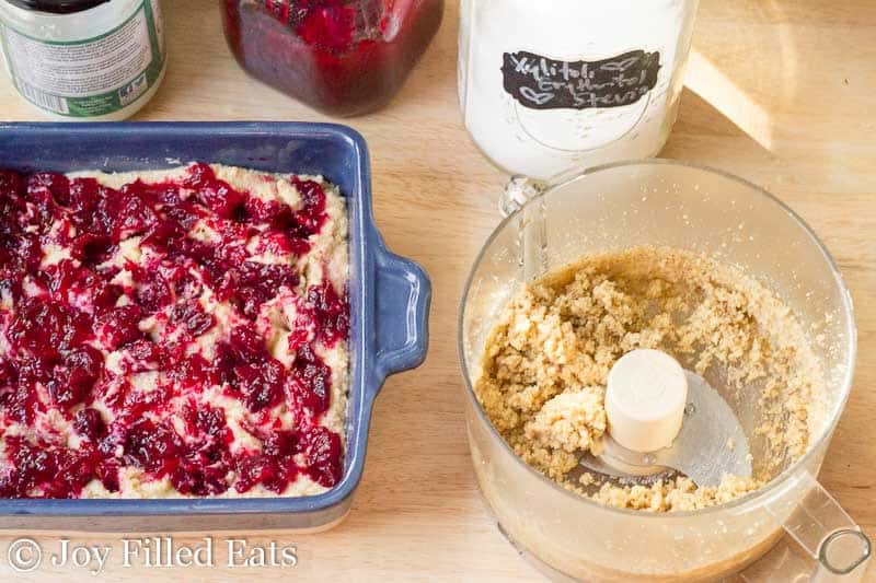 crumb topping inside a food processor next to a casserole dish with cranberry walnut cake batter