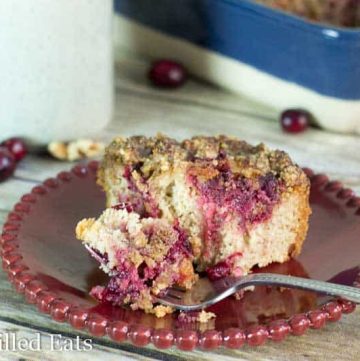 bite of cranberry walnut crumb cake on a fork resting on a a red plate with remaining crumb cake piece