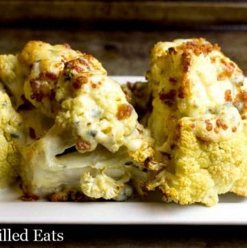 roasted cauliflower wedges on a white platter and topped with a blue cheese sauce and bacon pieces