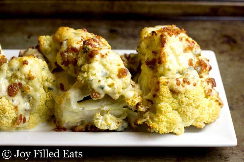 roasted cauliflower wedges on a white platter and topped with a blue cheese sauce and bacon pieces