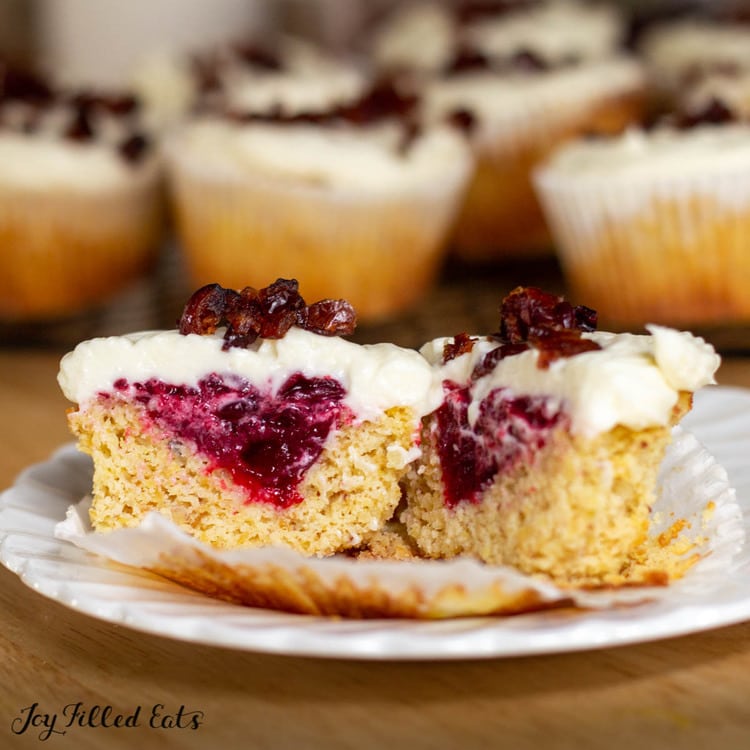 cranberry bliss cupcake sliced in half displaying interior jam on a white plate