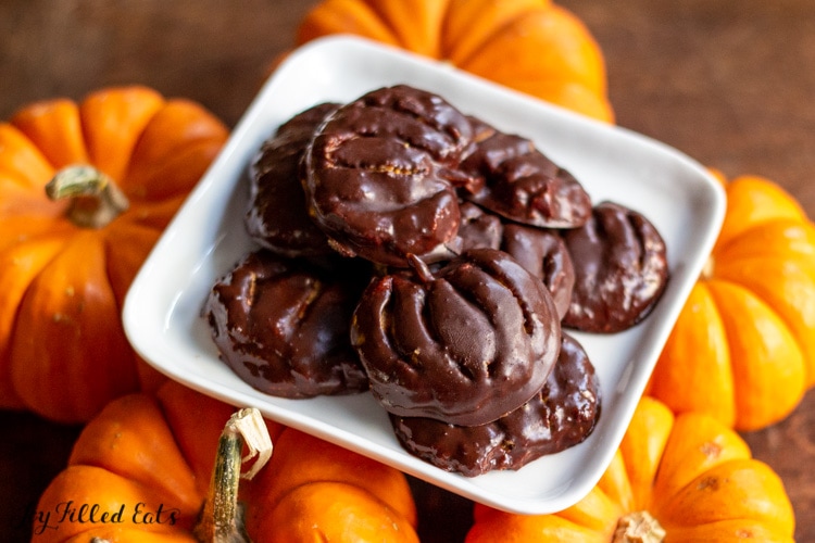 pile of sugar free peanut butter pumpkins on a square white plate placed on mini pumpkins