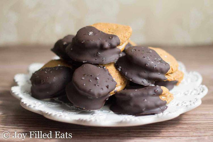 large pile of chocolate dipped peanut butter sandwich cookies on a white plate