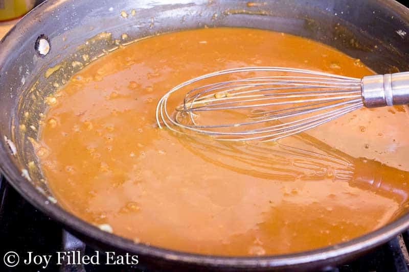 thai peanut sauce in a skillet being mixed with a whisk