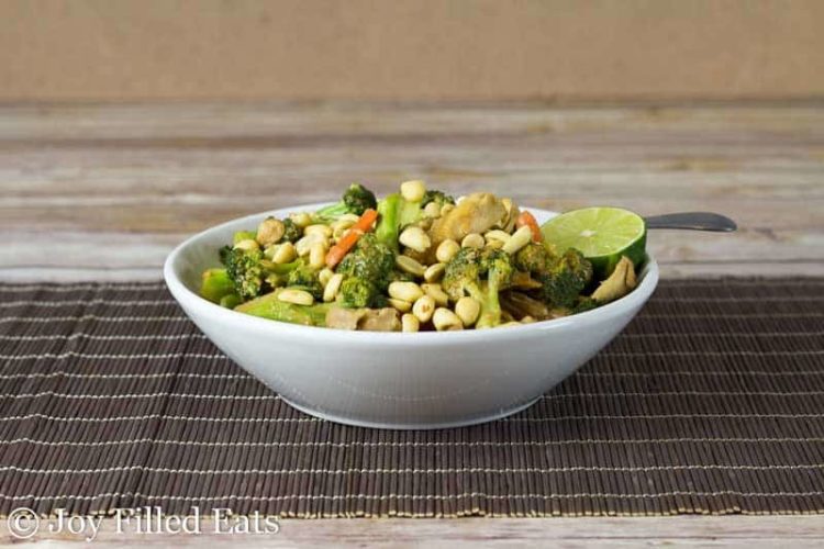 thai peanut chicken and broccoli in a white bowl set on a rustic place mat