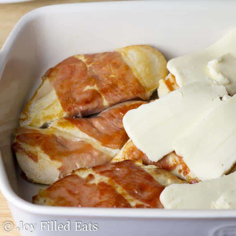 slices of cheese placed on top of prosciutto wrapped chicken breasts in a casserole dish