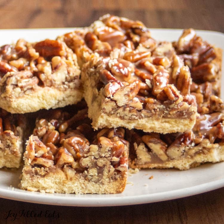 pile of pecan praline bars on a white plate from side