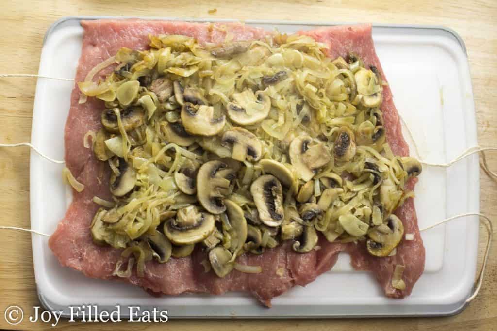 mushroom and onion filling layered on top of a butterflied pork roast laying on a cutting board