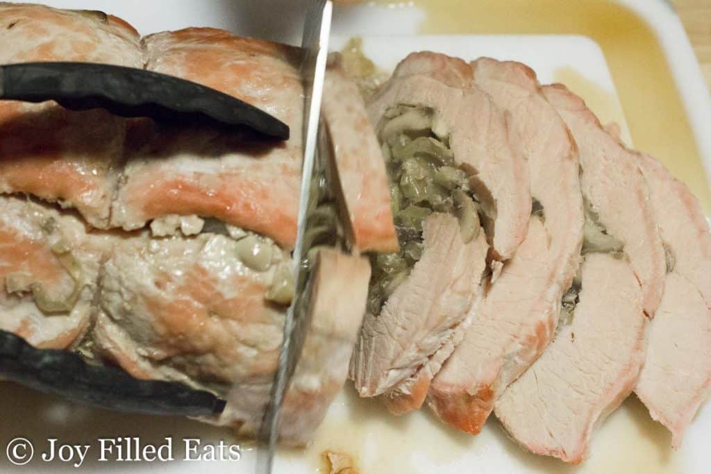 overhead view of chef's knife slicing stuffed pork marsala into thin pieces on a cutting board
