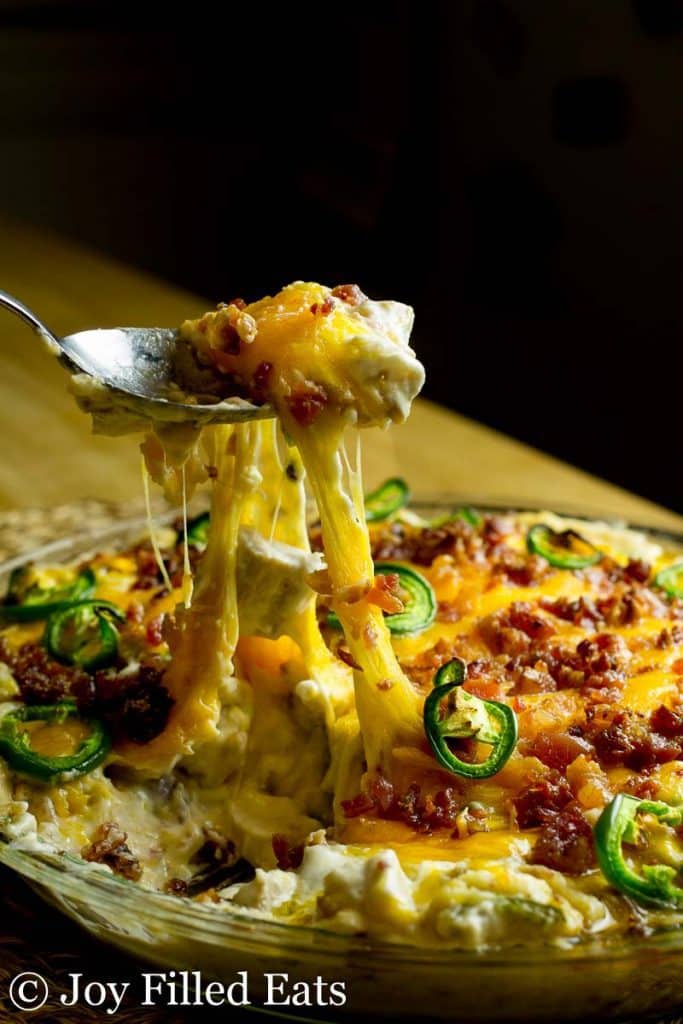 spoon lifting a serving of jalapeno popper dip from pie plate with gooey cheese