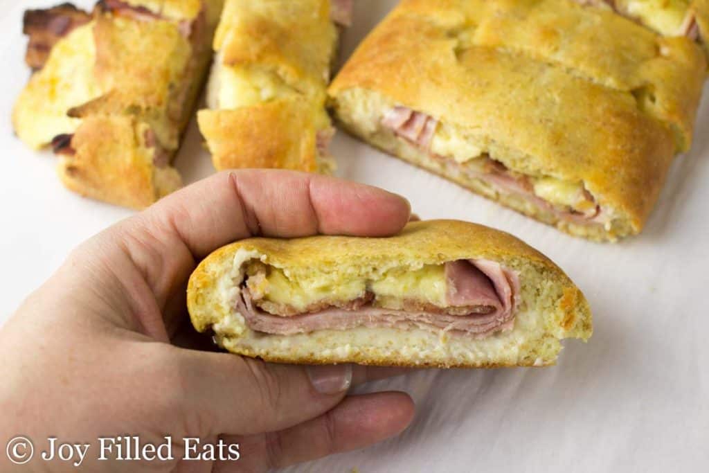 hand holding a slice of a loaded stromboli showing inside layers of meat and cheese