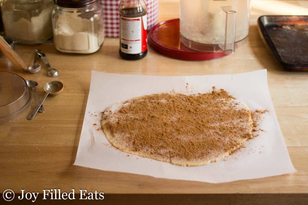 cinnamon sweetener filling covering cookie dough rolled out on parchment paper on a wooden table surface