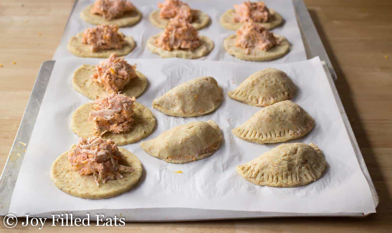 circle shaped dough topped with spicy chicken filling arranged on parchment lined sheet pan