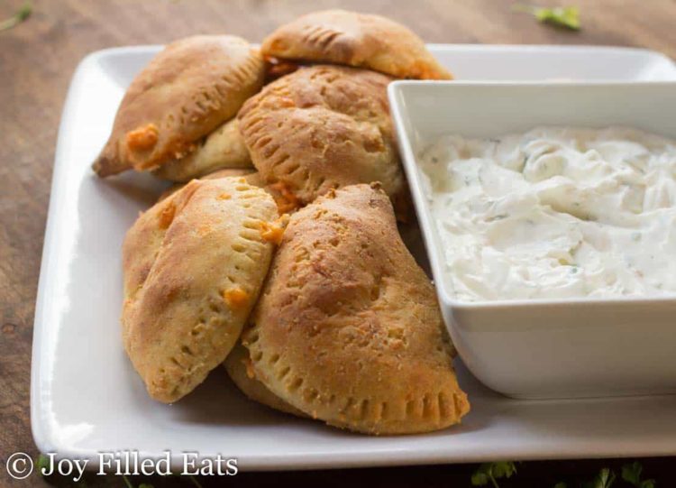pile of spicy chicken empanadas on a platter next to a small dish of cilantro sour cream