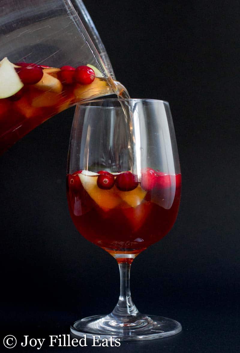 pitcher of apple cinnamon sangria being poured into a wine glass
