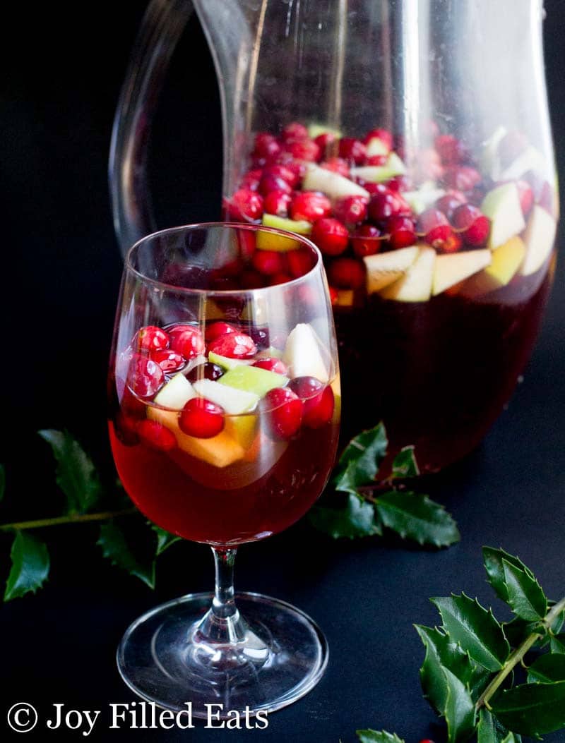 glass full of apple cinnamon sangria set in front of a pitcher full of sangria
