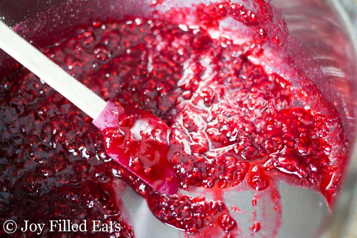 close up on raspberry puree in a saucepan being mixed with a spatula