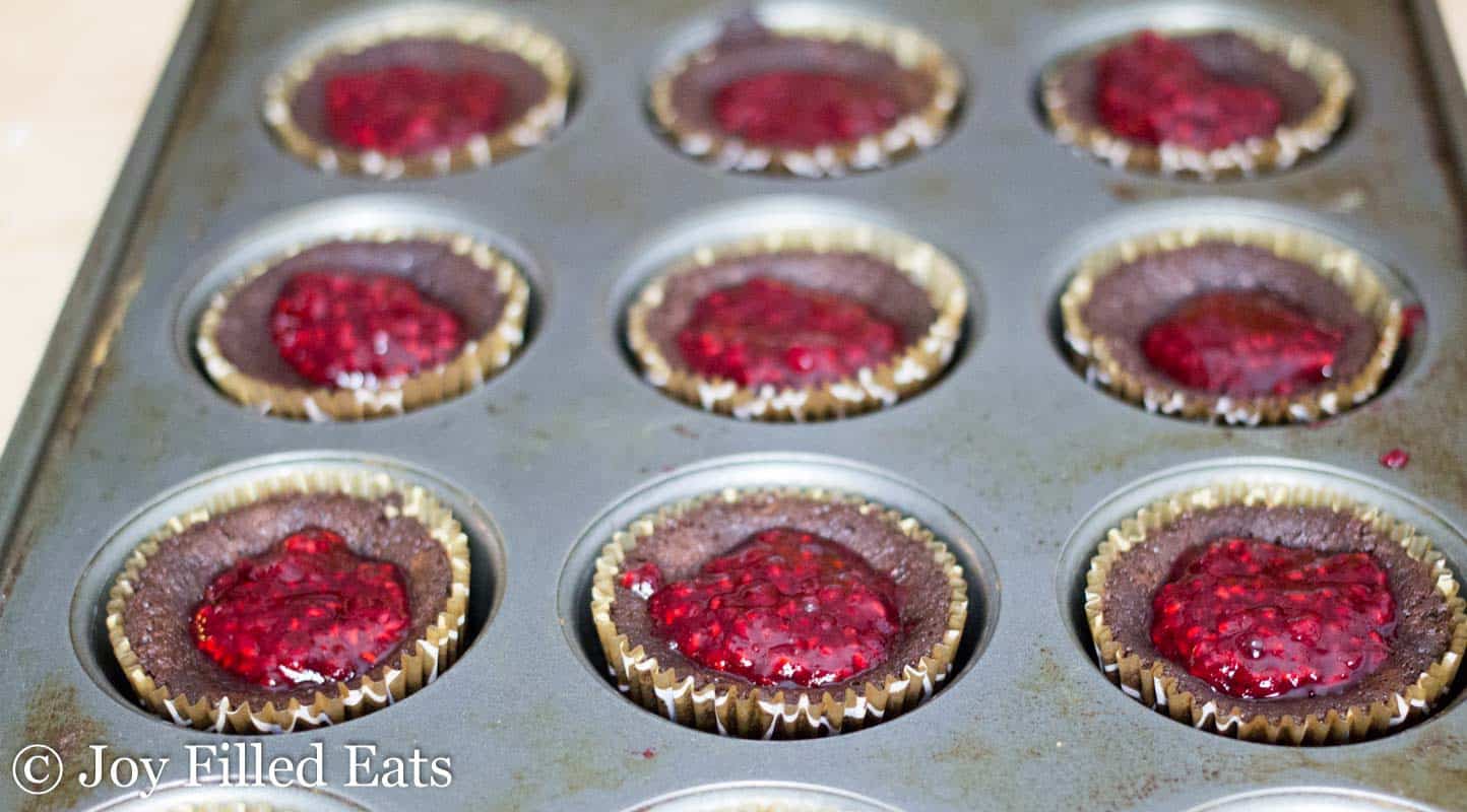 close up on muffin tin filled with chocolate champagne cupcakes topped with raspberry puree